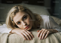 Portrait of a Young Woman with Blonde Hair and Blue Eyes Lying on a Beige Blanket