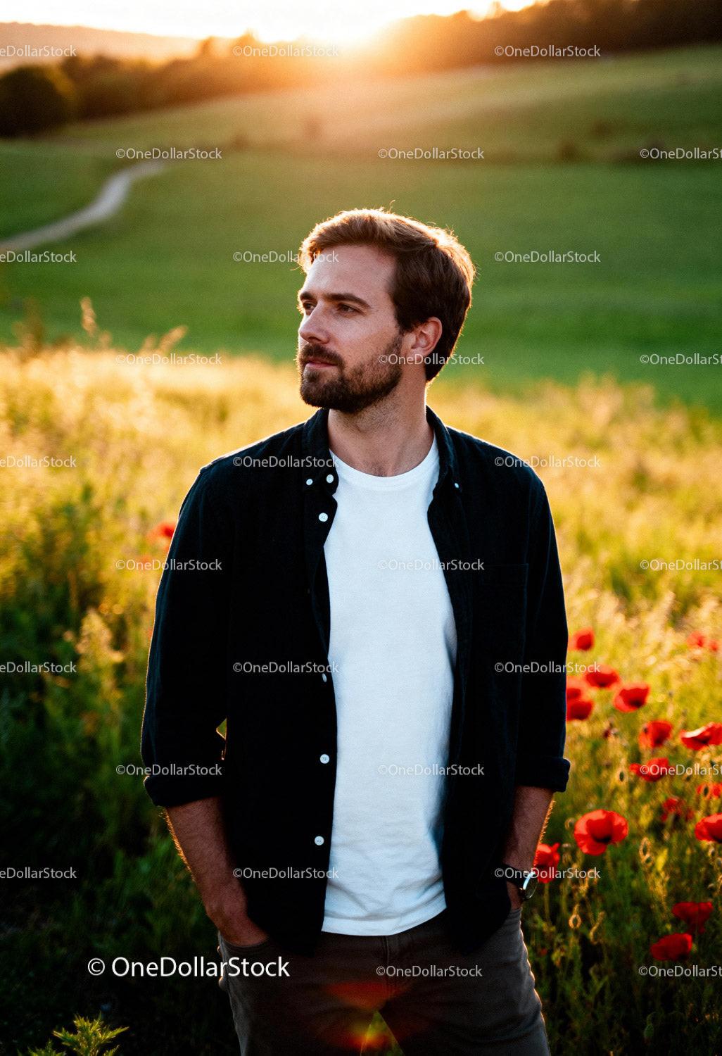 Thoughtful man standing in poppy field during sunset