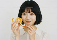 Young Woman Holding Fresh Orange Slice in Bright Minimalist Portrait