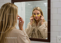 Woman Applying Under Eye Patches in Bathroom Mirror