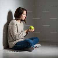 Young woman sitting on floor holding green apple