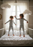 Two children jumping on bed in cozy striped pajamas