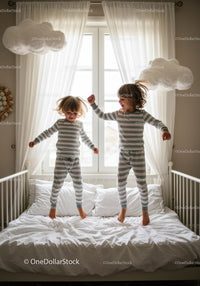Two children jumping on bed in cozy striped pajamas