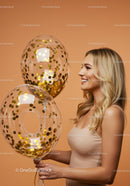 Smiling woman holding transparent balloons with gold confetti