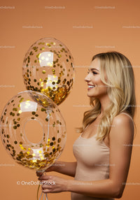 Smiling woman holding transparent balloons with gold confetti