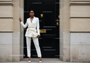 Confident woman in white suit posing against black door