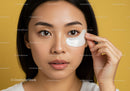 Young Woman Applying Eye Cream with Fresh Clear Skin Against Yellow Background