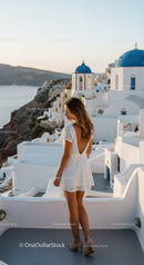 Woman in white dress overlooking Santorini cliffs
