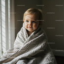Toddler wrapped in cozy blanket near bright window