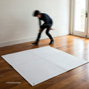 Blurred figure inspecting large white grid on wooden floor