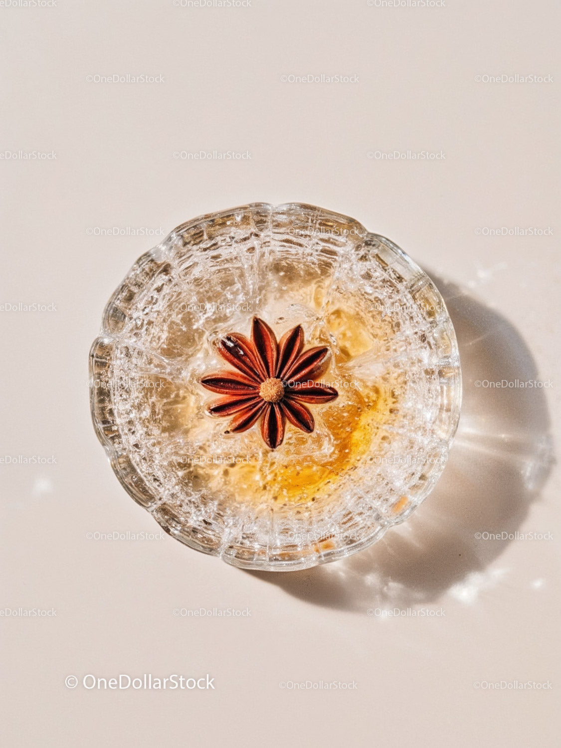 Glass bowl with ice and star anise on light surface