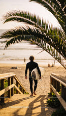 Surfer walking to the beach with surfboard at sunset