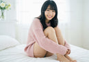 Smiling Young Woman Sitting on Bed in Cozy Pink Sweater