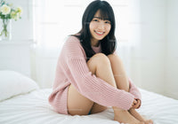 Smiling Young Woman Sitting on Bed in Cozy Pink Sweater