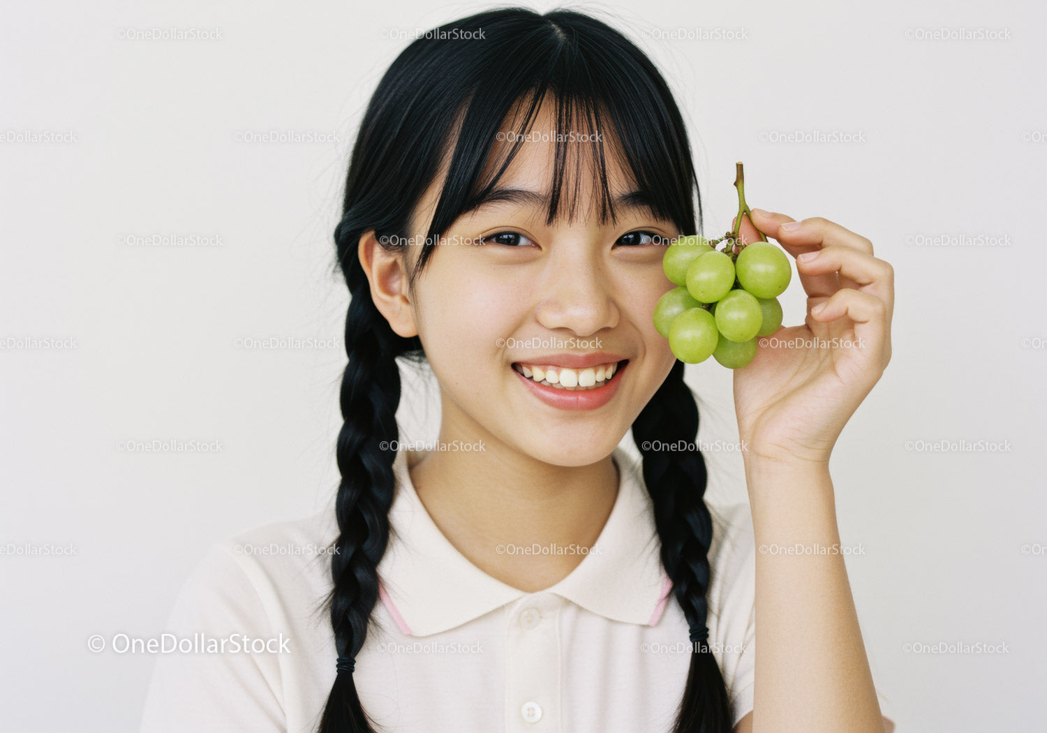 Smiling Girl with Black Braided Hair Holding Green Grapes