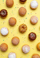 Assorted colorful donuts with sprinkles on yellow background