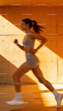 Active woman jogging fast by urban wall at sunset