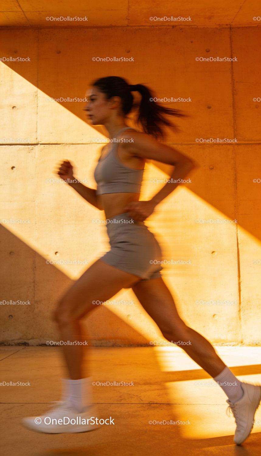 Active woman jogging fast by urban wall at sunset