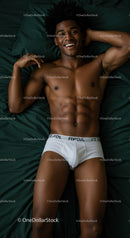 Smiling young man relaxing shirtless on dark bedding