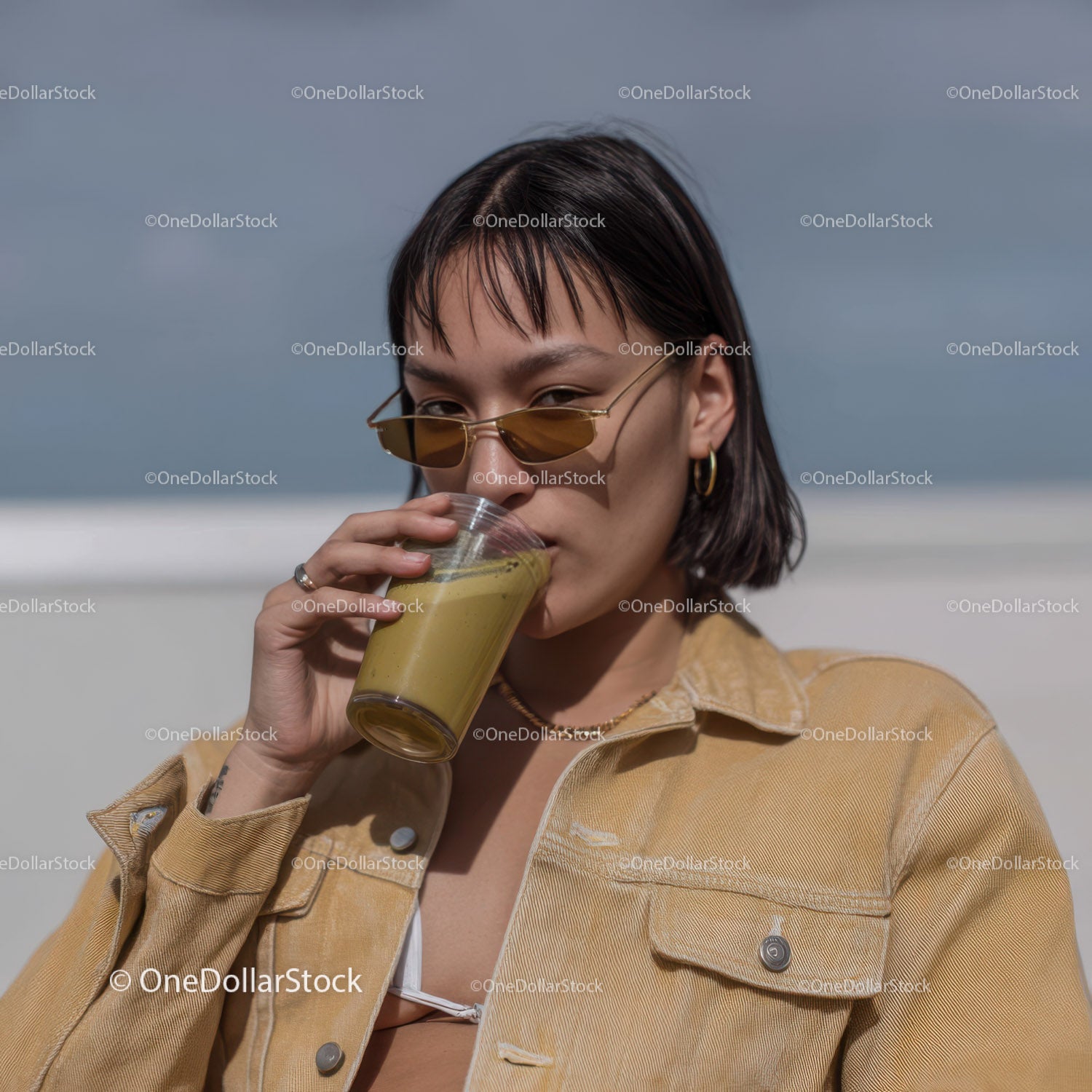 Chic Woman Drinking Green Smoothie with Beach Ocean Background