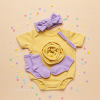 Yellow Baby Onesie with Lilac Accessories on Beige Background