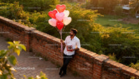 Man holding heart-shaped balloons and chocolates outdoors