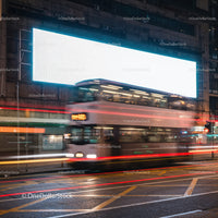 Double-decker bus speeding past illuminated city billboard