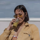 Young woman in beige jacket drinking smoothie on city street