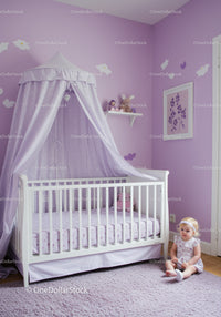 Cute Baby Girl Sitting Near White Crib in Lavender Nursery