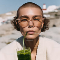 Stylish Woman with Short Hair and Large Sunglasses Drinking Green Juice at Beach