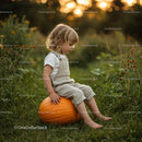Child sitting thoughtfully on pumpkin in green field