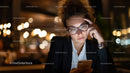 Confident Woman with Curly Hair Reading Smartphone in Night Cafe