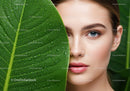 Close-Up of Woman with Blue Eyes Behind Large Green Leaf with Dew Drops