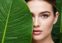 Close-Up of Woman with Blue Eyes Behind Large Green Leaf with Dew Drops
