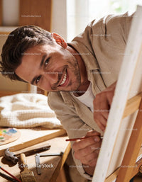 Smiling man focused while painting on canvas indoors