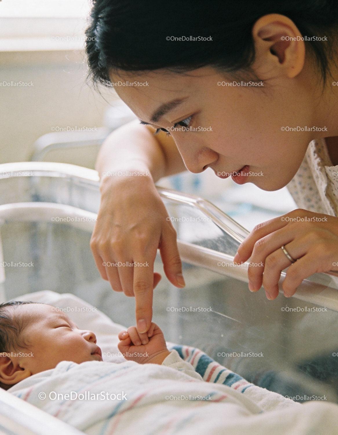 Mother Tenderly Holding Newborns Finger in Hospital Crib
