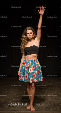 Young woman in floral skirt raising hand confidently
