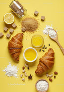 Fresh croissants with baking ingredients on yellow surface