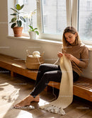 Woman knitting a cozy white scarf in a sunlit room