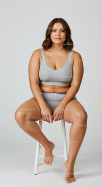 Confident plus size woman in gray workout outfit sitting on a stool