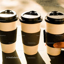 Three Disposable Coffee Cups with Black Sleeves on Table