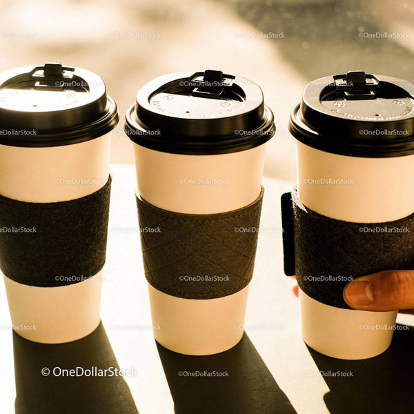 Three Disposable Coffee Cups with Black Sleeves on Table