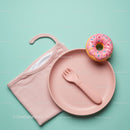 Pink baby plate with spork and toy donut on blue background