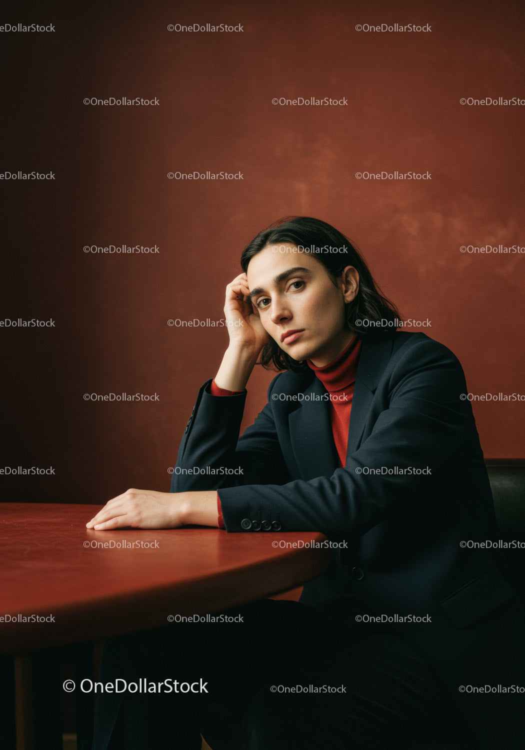 Elegant Woman in Business Suit Sitting at Table Against Brown Background