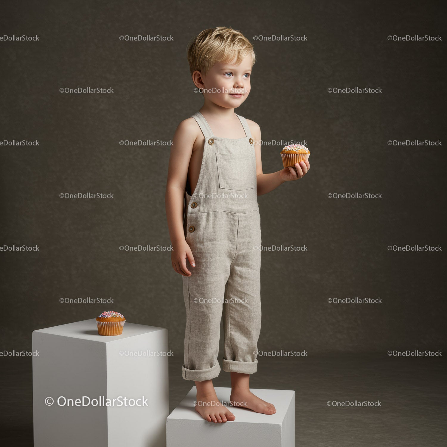 Blond toddler holding cupcake standing on white cube