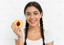 Young Woman Holding Peach Slice with Bright Smile in Studio