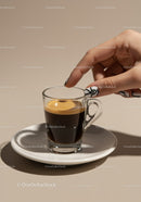 Hand Reaching for Glass Espresso on White Saucer