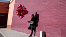 Man Holding Heart Balloons and Chocolates by Brick Wall