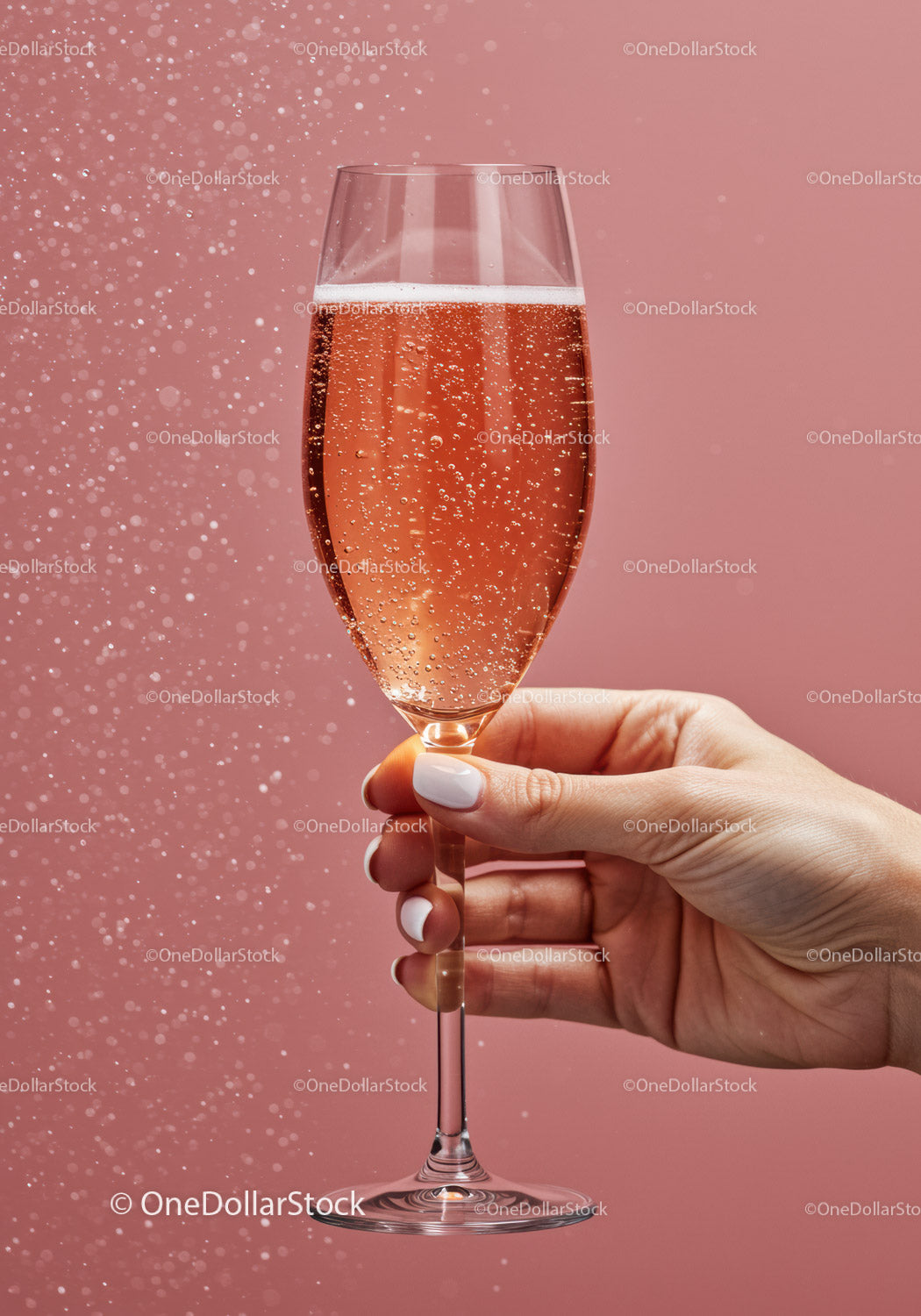 Hand holding sparkling rose champagne glass on pink background