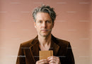 Elegant Mature Man in Brown Blazer Holding Notebook Against Neutral Background